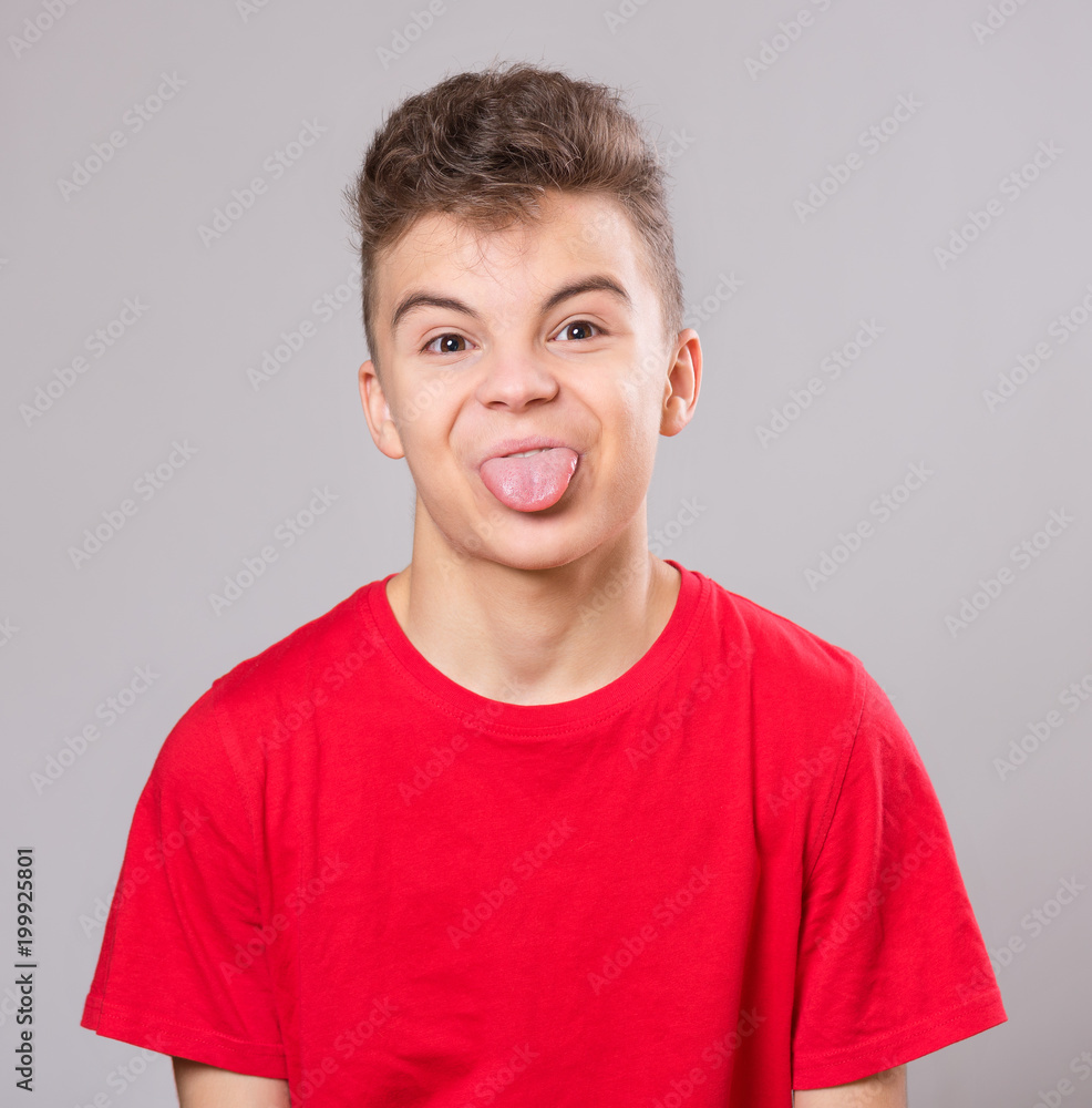 Emotional portrait of cut teen boy showing his tongue. Funny teenager puts out tongue, on gray background. Emotional portrait of cut teen boy showing his tongue. Funny teenager puts out tongue, on gray background.