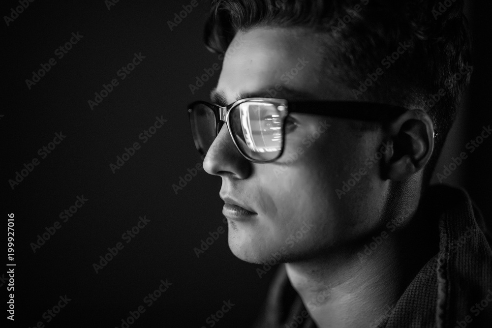 Close up of man face. Eyes of serious young man in black rim glasses using his tablet computer. Screen and finger reflecting in the glass. Gray photo. Close up of man face. Eyes of serious young man in black rim glasses using his tablet computer. Screen and finger reflecting in the glass. Gray photo.
