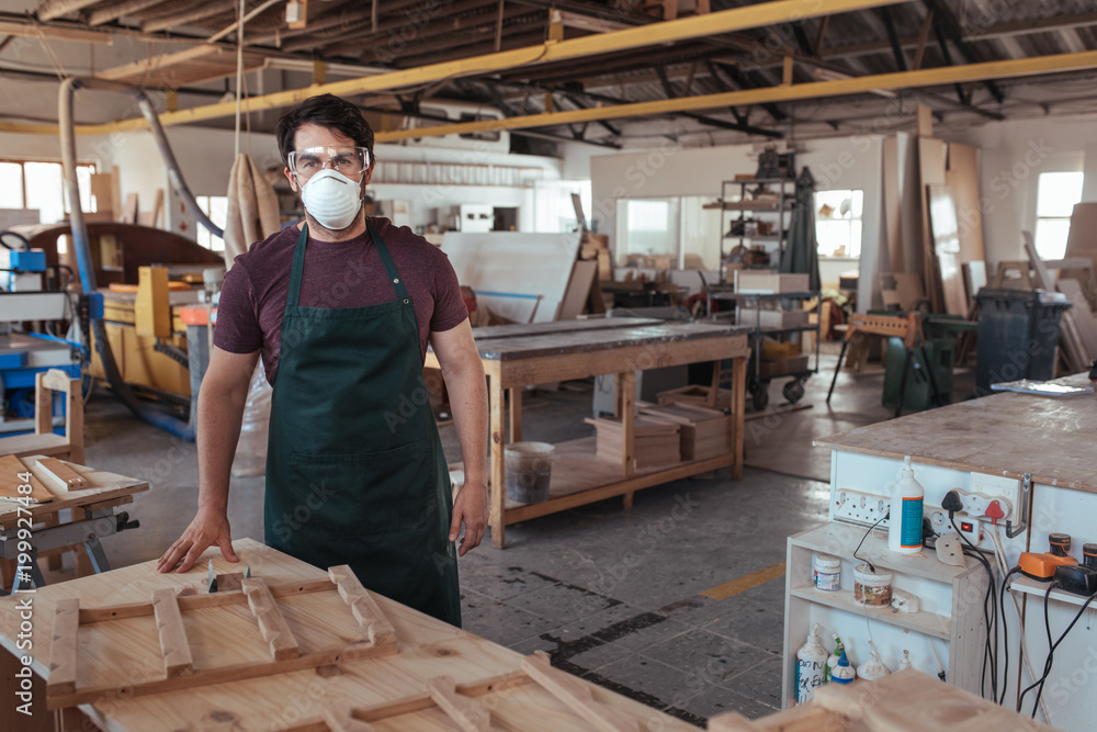 Young woodworker standing in his studio wearing protective workwear Young woodworker standing in his studio wearing protective workwear