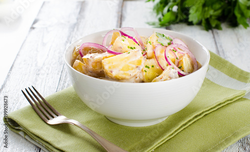 Fresh potato salad with mayonnaise dressing, onion and capers on white wooden background