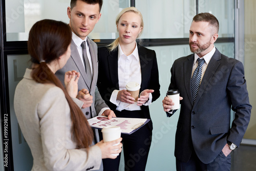 Group portrait of business team discussing work standing in hall of modern office building at coffee break holding cups