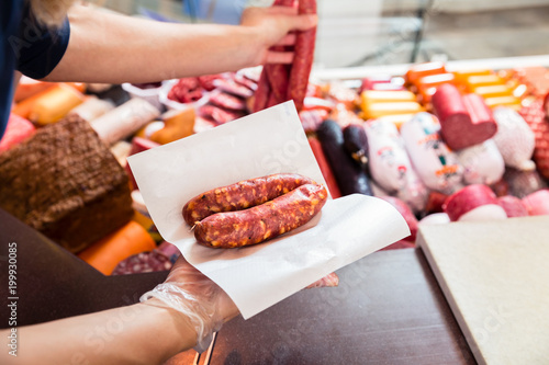 Fotografie Sales woman in butchery holding sausage wrapped in paper, close-up