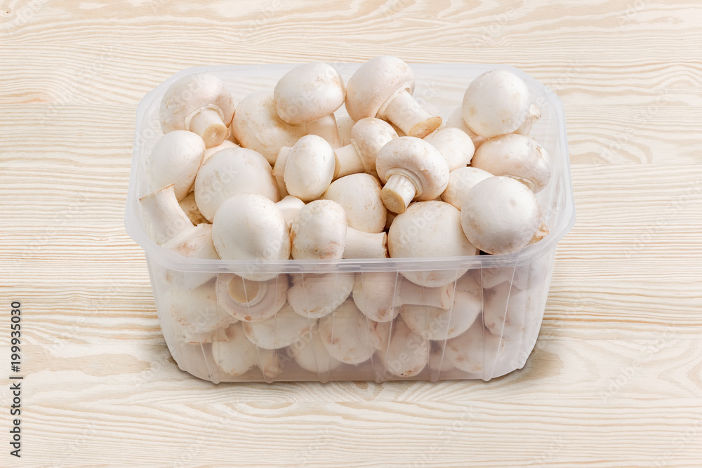 White button mushrooms in the plastic container on wooden surface White button mushrooms in the plastic container on wooden surface