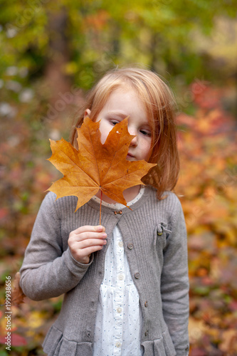 The girl is holding a yellow maple leaf
