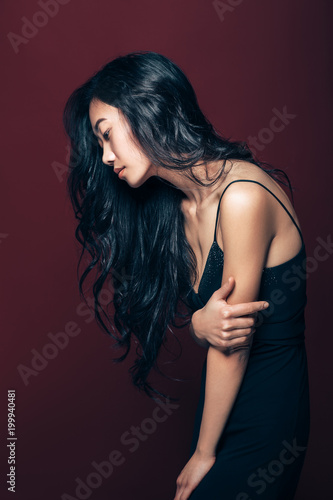 Profile portrait of beautiful asian woman in black dress posing in studio