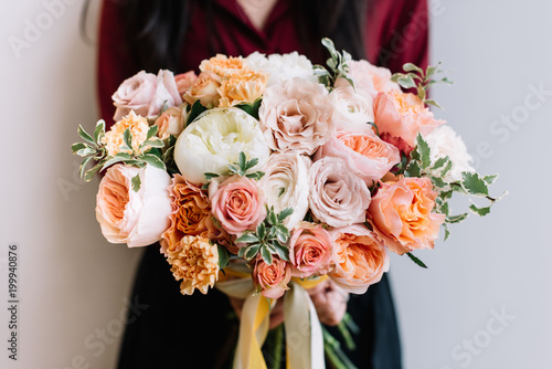 Very nice young woman holding big and beautiful colourful flower wedding bouquet of David Austin roses, ranunculus, peach campanella roses and pistachios photo