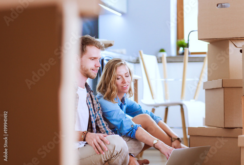 Young couple moving in new home.Sitting and relaxing after unpacking.Looking something on laptop. Young couple
