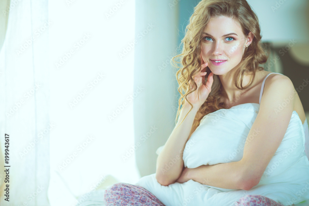 Young woman holding a pillow while sitting on her bed. Young woman holding a pillow while sitting on her bed.