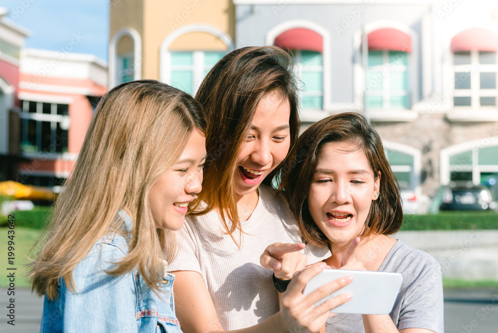 Obraz premium Group of young Asian Women selfie themselves with a phone in a pastel town after shopping. Young women group do outdoor activity under the blue sky. Outdoor activity after shopping concept.