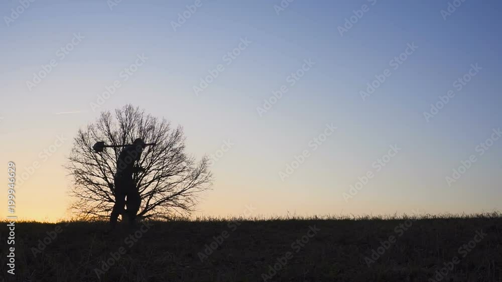 Stfarmer with a shovel walking on the field. They carry equipment for planting a tree. On the Sunset. Side view Stfarmer with a shovel walking on the field. They carry equipment for planting a tree. On the Sunset. Side view