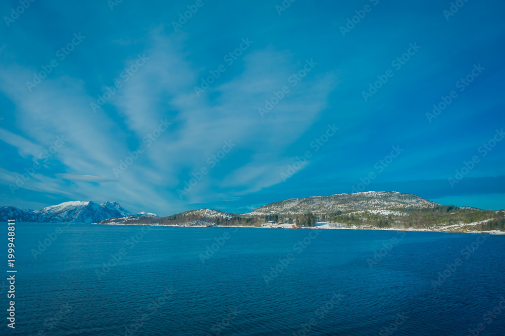 Beautiful outdoor view of coastal scenes of huge mountain covered with snow on Hurtigruten voyage