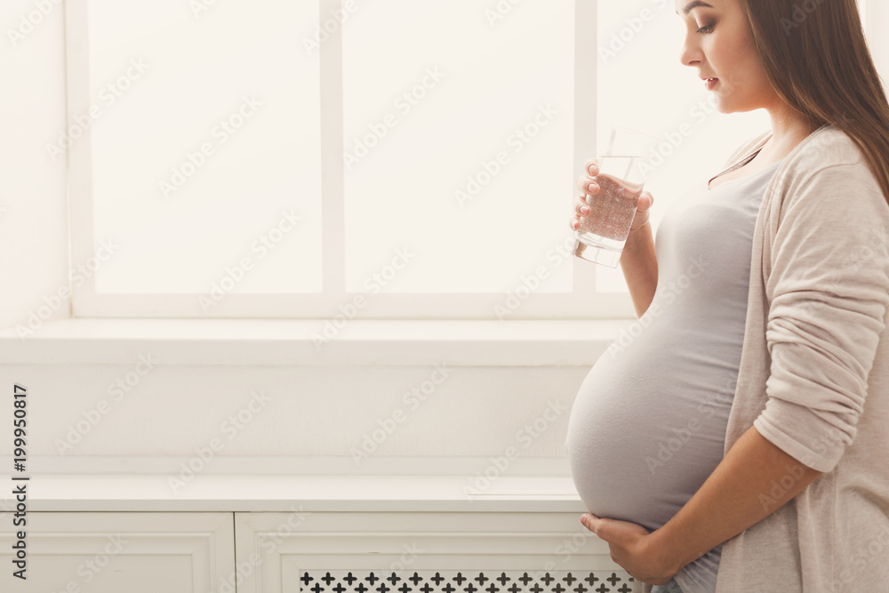Pregnant woman drinking water at window