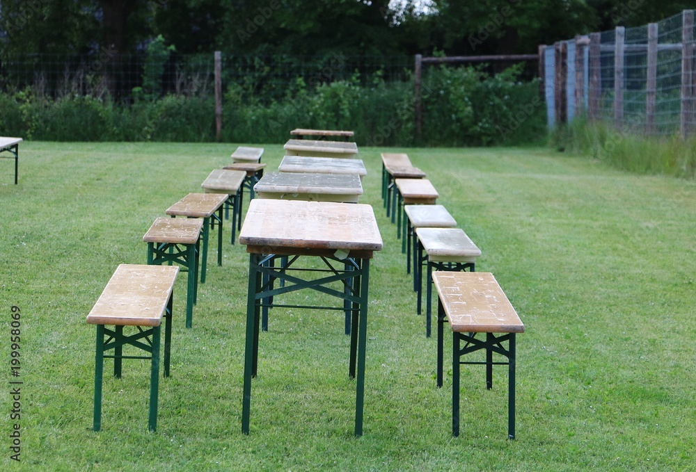 party tables and benches are standing in the garden in a row