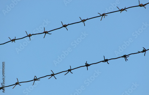Old rusty mono-basic barbed wire in two lines on a clear blue sky