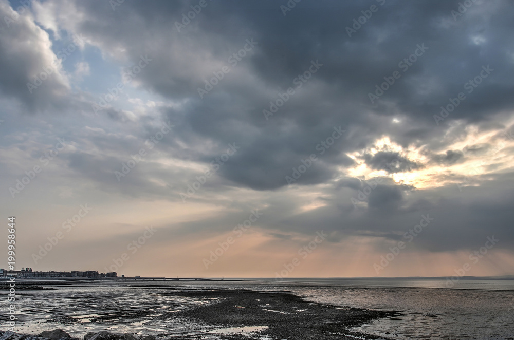 Dramatic cloudscape over the black sands and mudflats in the bay of Morecambe, with the town of Morecambe in the distance