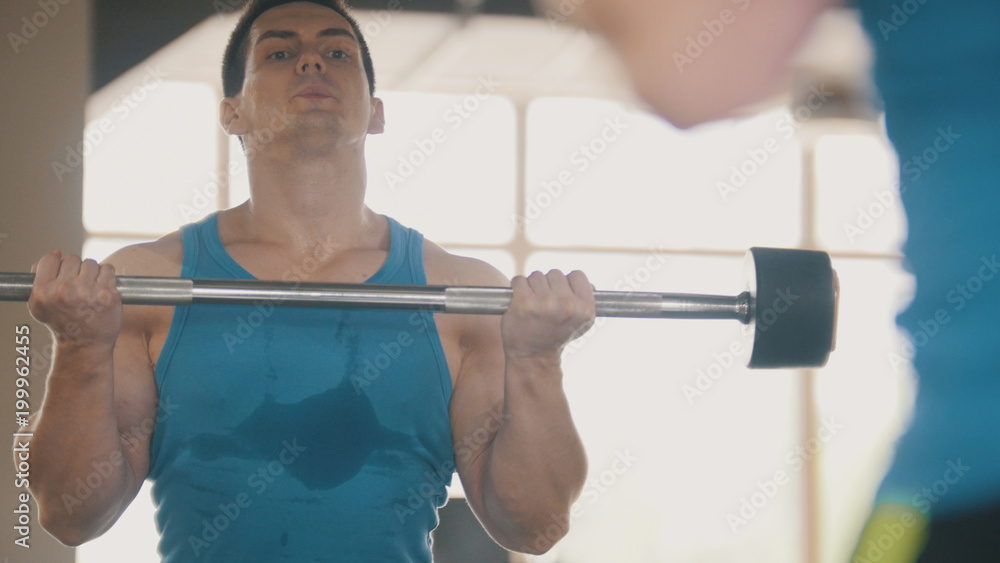 Muscular man in the gym with sports rod in front of mirror