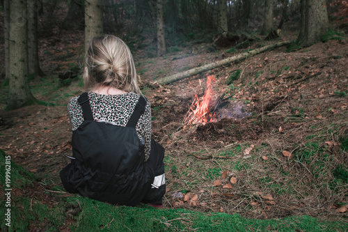 Young girl in the forest sitting by the bonfire for warmth and safety photo