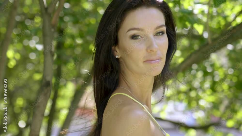 Portrait of natural beautiful young brunette woman smiling and looking at camera on the summer street. Slow motion. HD Portrait of natural beautiful young brunette woman smiling and looking at camera on the summer street. Slow motion. HD