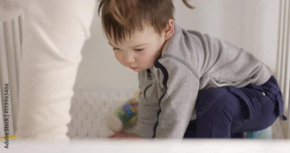 Mother picking up toys from crib as sleepy child watches Mother picking up toys from crib as sleepy child watches