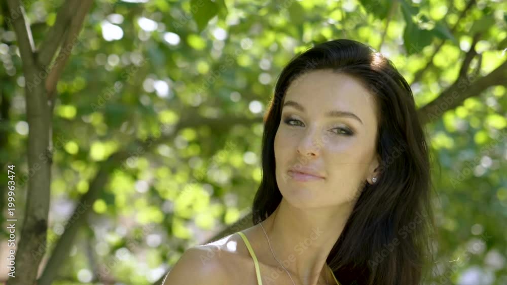 Portrait of natural beautiful young brunette woman smiling and looking at camera on the summer street. Slow motion. HD Portrait of natural beautiful young brunette woman smiling and looking at camera on the summer street. Slow motion. HD