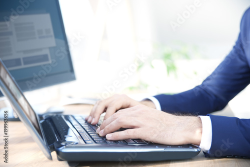 Close-up shot of businessman s hands while typing on keyboard. Professional man wearing suit while sitting at office desk and workin on laptop.