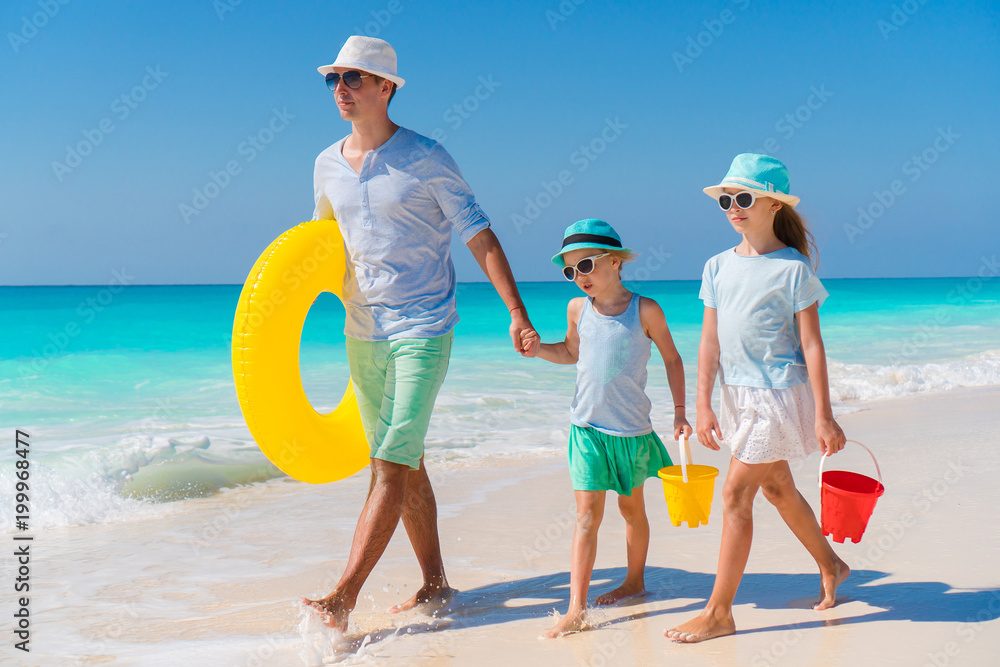 Family of dad and kids walking on white tropical beach on caribbean island with beach toys. Family beach holidays Family of dad and kids walking on white tropical beach on caribbean island with beach toys. Family beach holidays