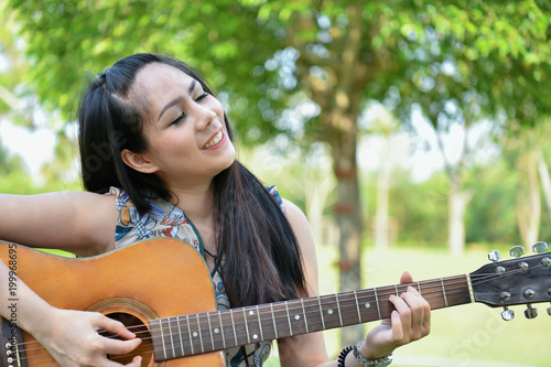 Music Concepts. Asian girls playing guitar. Asian women relaxing with music. Asian women have a happy lifestyle. Beautiful Asian girl playing guitar in the garden.