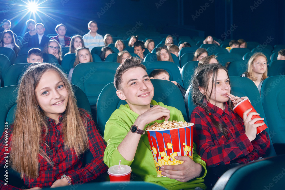 frontview of happy children eating popcorn by watching movie. Girl drinking fizzy drink from red can. Children watching new film or cartoon. looking interested and exited. Wearing colorful shirt.