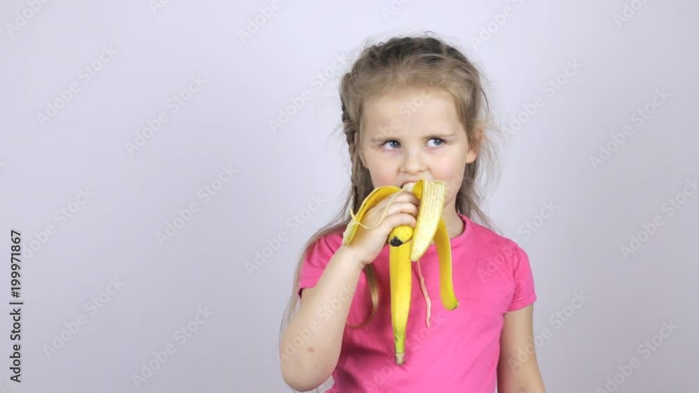 A young girl bites a banana and shows her thumb up A young girl bites a banana and shows her thumb up