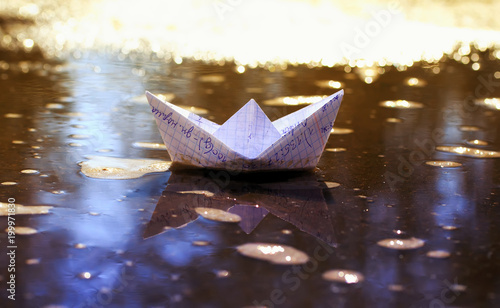 school small paper boat from a cellular notebook floats in the Sunny spring early puddle