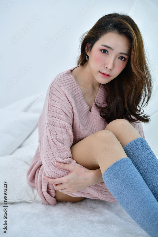 Winter Concept. Cute Asian girl in winter dress. Beautiful woman is  relaxing in a white bedroom. Beautiful women in winter clothes are relaxing  in the morning. Stock Photo