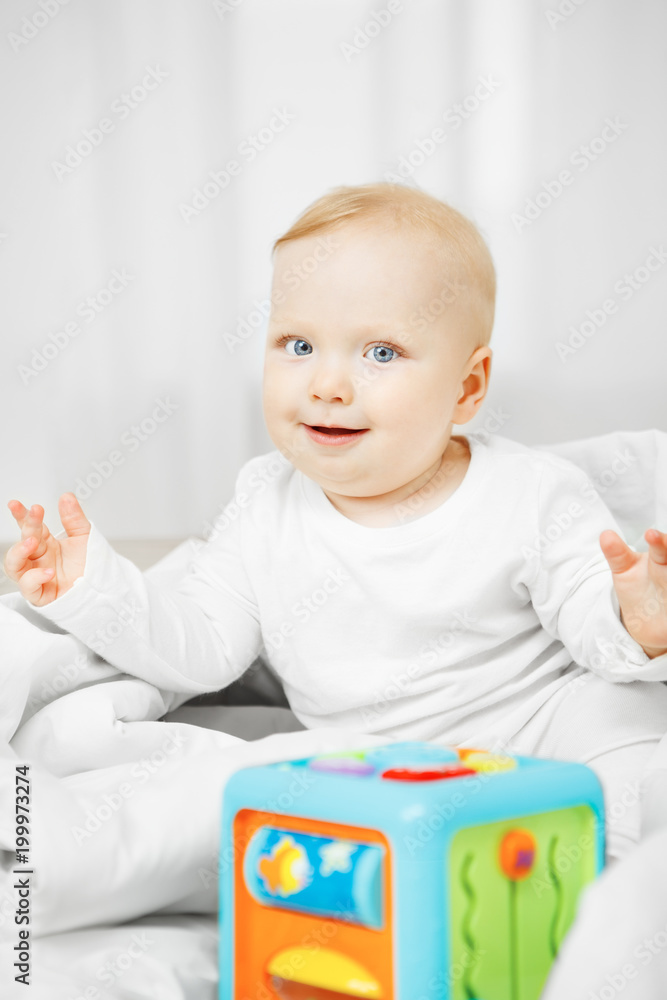Adorable playful baby sits on bed with cubic toy Adorable playful baby sits on bed with cubic toy
