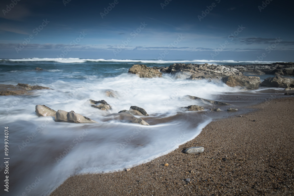scenic atlantic coastline with waves in motion around rocks on sandy beach in long exposure, bidart, basque country, france