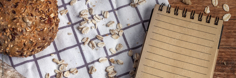 Panoramic wooden view on table with bread, rolls, oat flakes and a notebook on checkered material