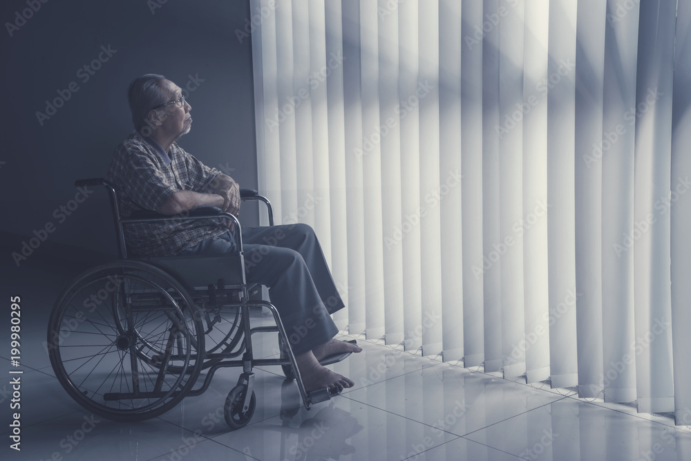 Old man sits on wheelchair while daydreaming Old man sits on wheelchair while daydreaming