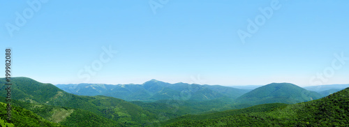 Beautiful panoramic mountain landscape, low hills and mountain peaks covered with green forestt, blue sky. Skyline, Markhotsky Range, Russia