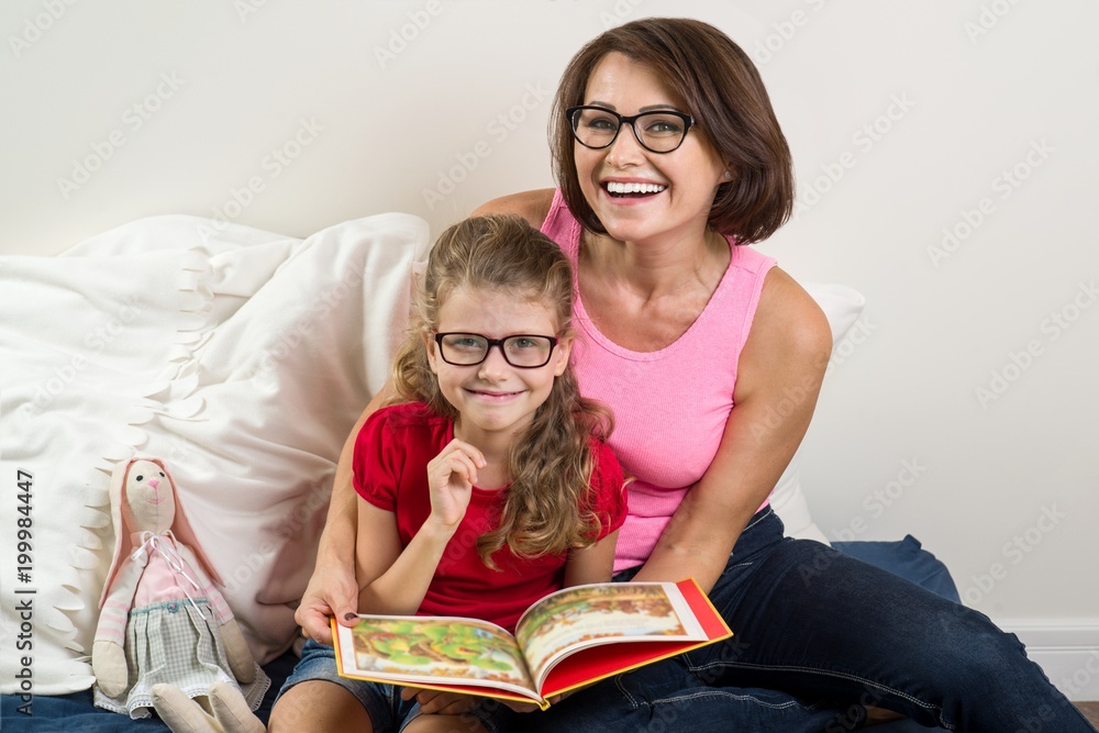 Mom and little daughter read book at home in bed. Mom and little daughter read book at home in bed.