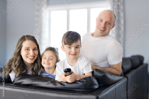 Family sitting in living room with remote control smiling © Louis-Photo