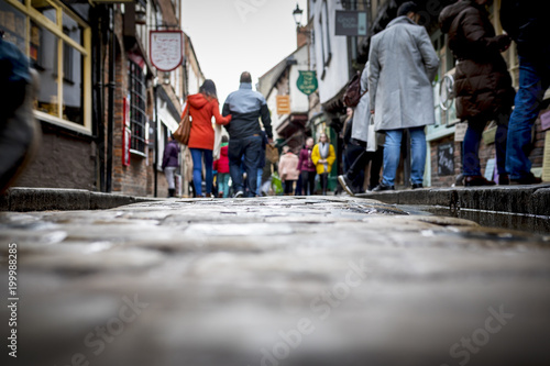 Low down shot of people and couple walking holding hands down a old traditional cobbled English street whilst browsing in shops on retail therapy day