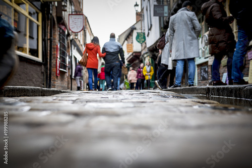 Low down shot of people and couple walking holding hands down a old traditional cobbled English street whilst browsing in shops on retail therapy day photo