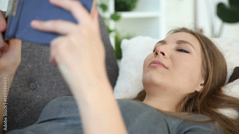 A European-looking girl reads a book at home at home on a gray sofa in the living room A European-looking girl reads a book at home at home on a gray sofa in the living room