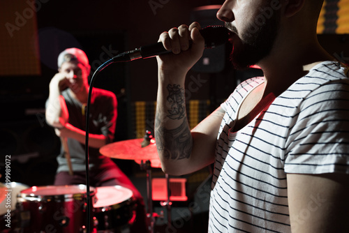 Side view close up of tattooed hip-hop singer with his music band performing in dim recording studio, copy space