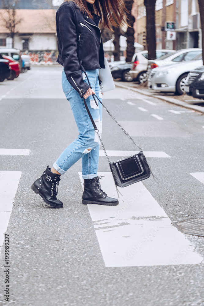fashion blogger outfit details. fashionable woman wearing ripped vintage denim  jeans, suede jacket, black biker boots -ankle shoes and black trendy  handbag. detail of a perfect fall fashion outfit. Photos | Adobe