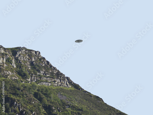 UFO Sighting, flying saucer in the sky over hills on summers day, metal flying spacecraft