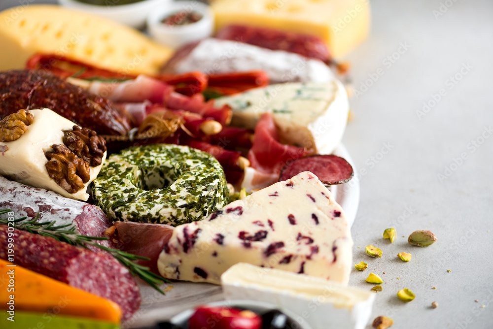 Traditional italian antipasto, cutting board with salami, cold smoked meat, prosciutto, ham, cheeses, olives, capers on grey background. Cheese and meat appetizer