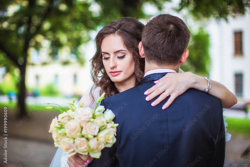 Bride hugs groom by shoulders, holding in her hand wedding bouquet of roses Bride hugs groom by shoulders, holding in her hand wedding bouquet of roses