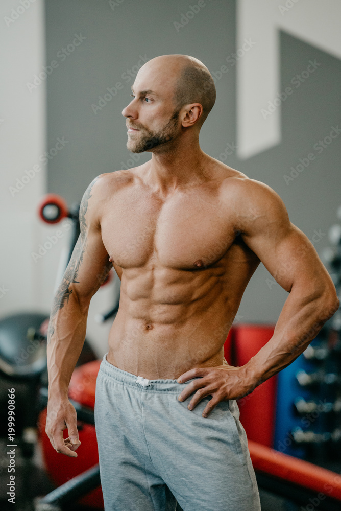 Shredded shirtless tough bodybuilder with beard watching to the left side, posing in a gym. Shredded shirtless tough bodybuilder with beard watching to the left side, posing in a gym.