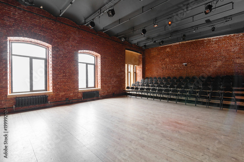 Loft style. Hall with black chairs for webinars and conferences. A huge room with large Windows  surrounded by brickwork  and parquet floors. For film and theatre productions