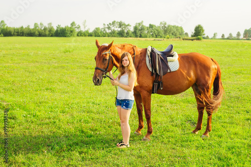 a teenage girl stands by a beautiful brown horse and looks at the camera lens