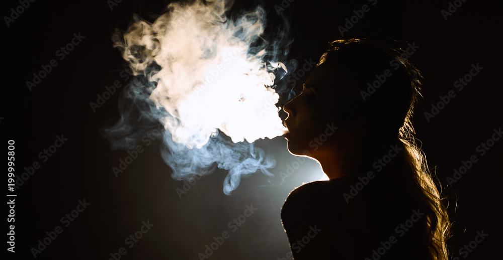 Beautiful young woman profile in backlight smoking hookah with a lot of smoke isolated black background. Club party menu concept